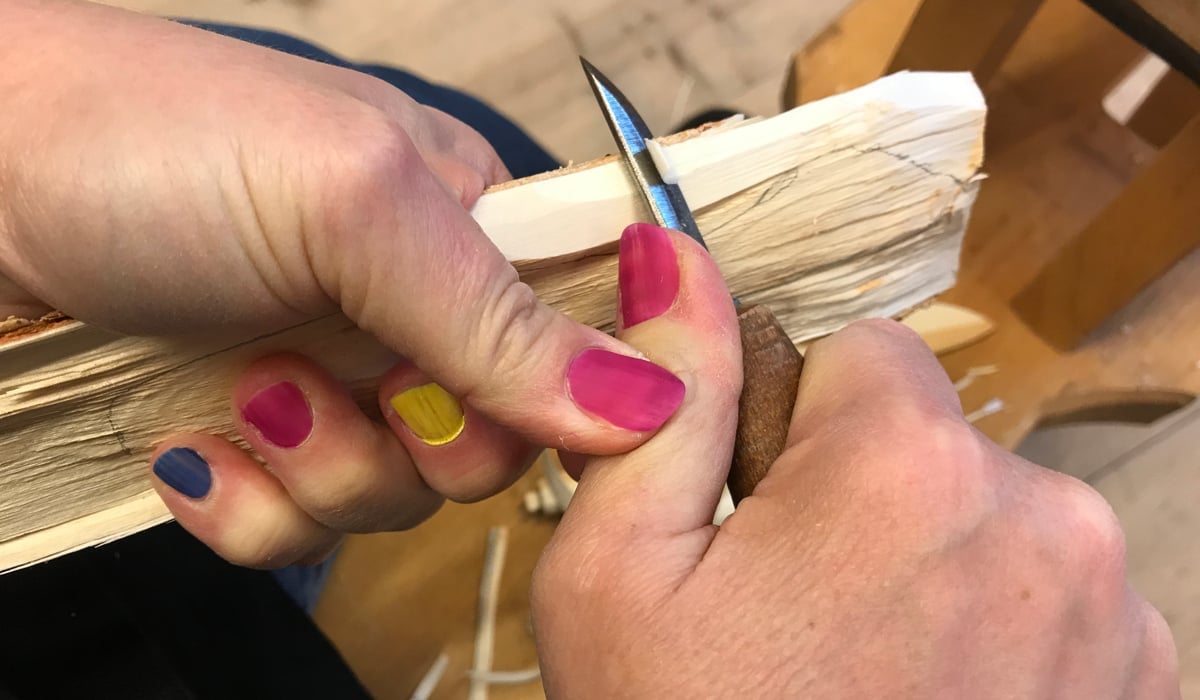 Händer som täljer med kniv, fingrarna har naglar målade i olika färger