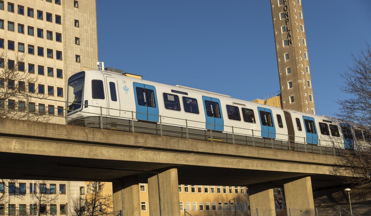 Tunnelbanetåg av modell C30 färdas över en bro. Blå himmel och kontorsbyggnad i bakgrunden.