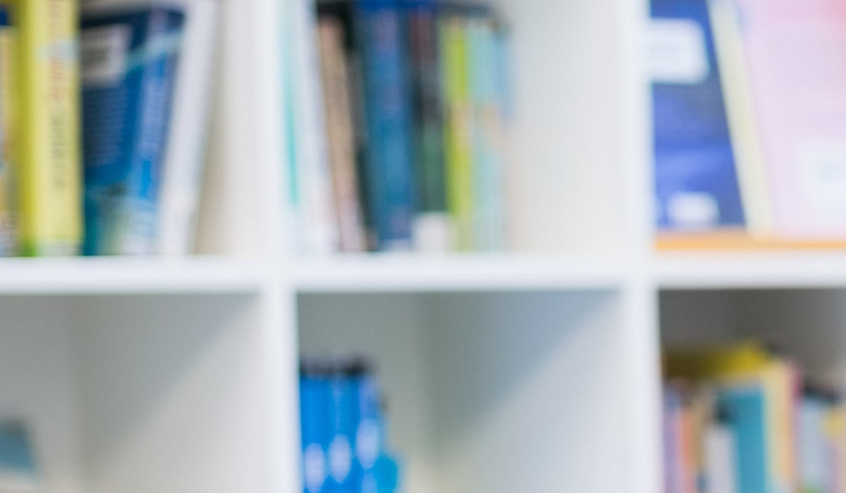 Flicka i rullstol läser en bok i ett skolbibliotek