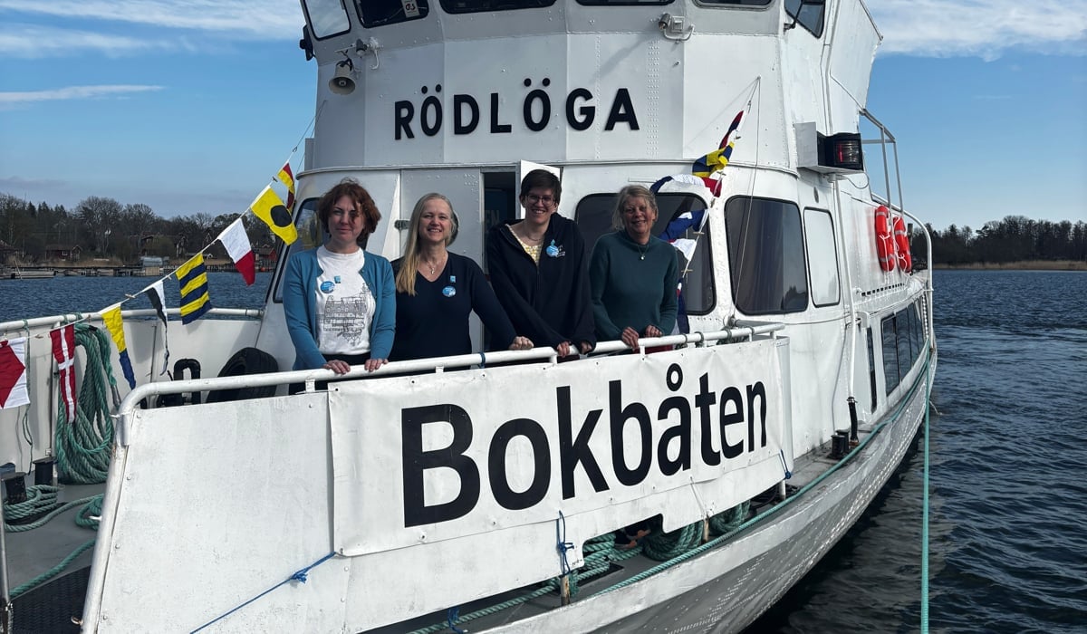 En grupp människor på en båt i vattnet. Båten har en dekal med namnet bokbåten.