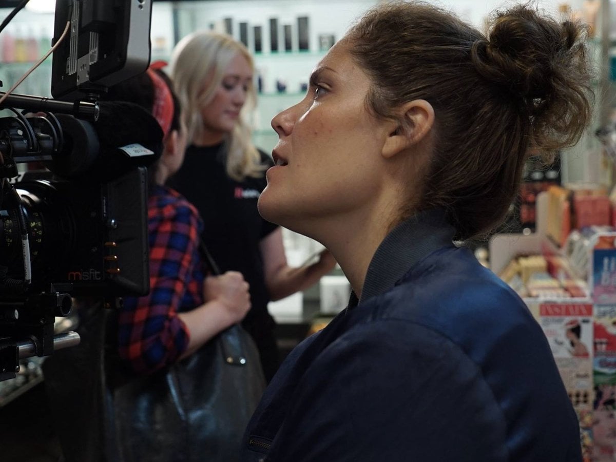 En kvinna med en filmkamera i en affär. Två unga kvinnor står och pratar.