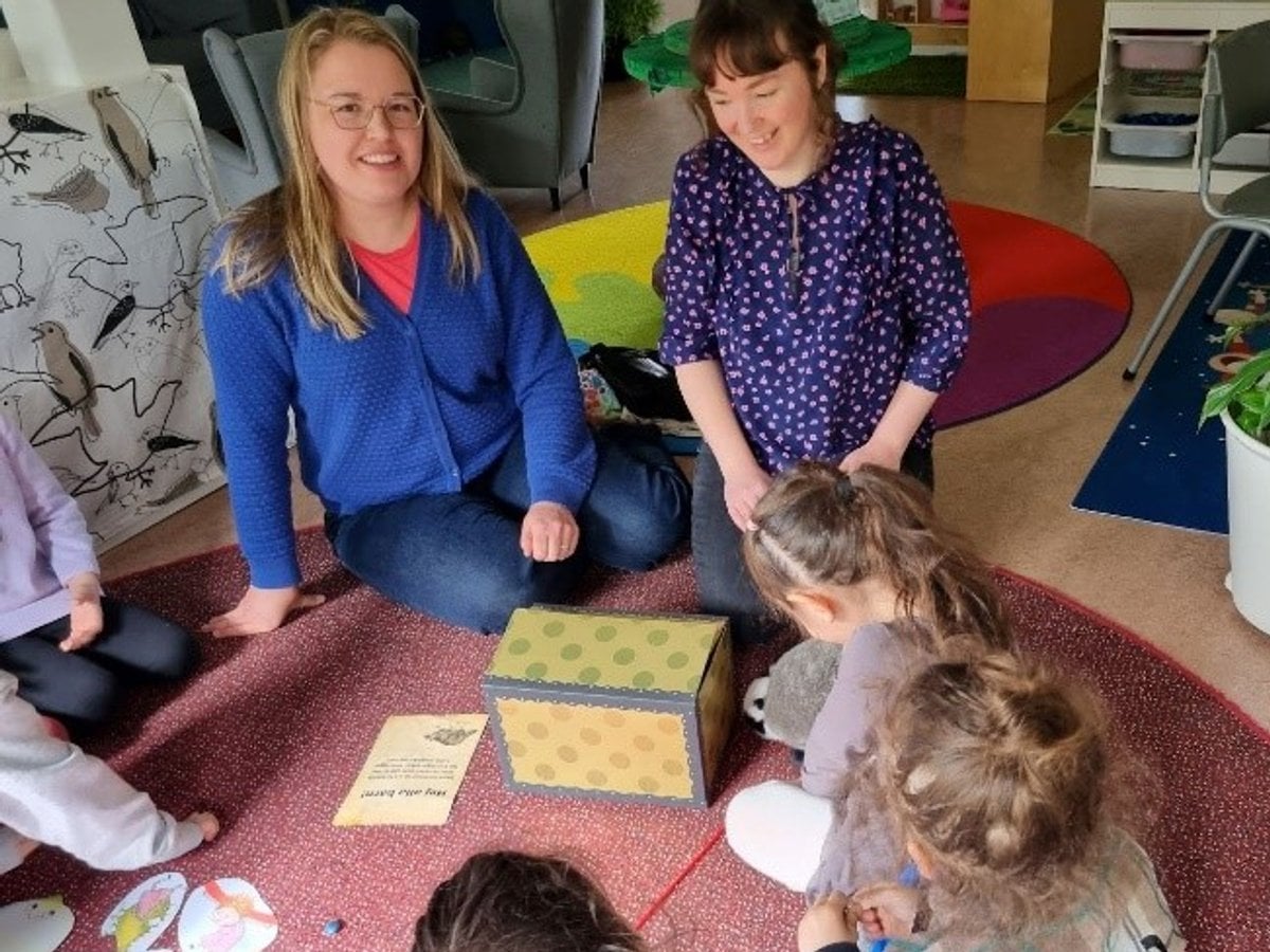Två bibliotekarier sitter med en grupp barn på en matta