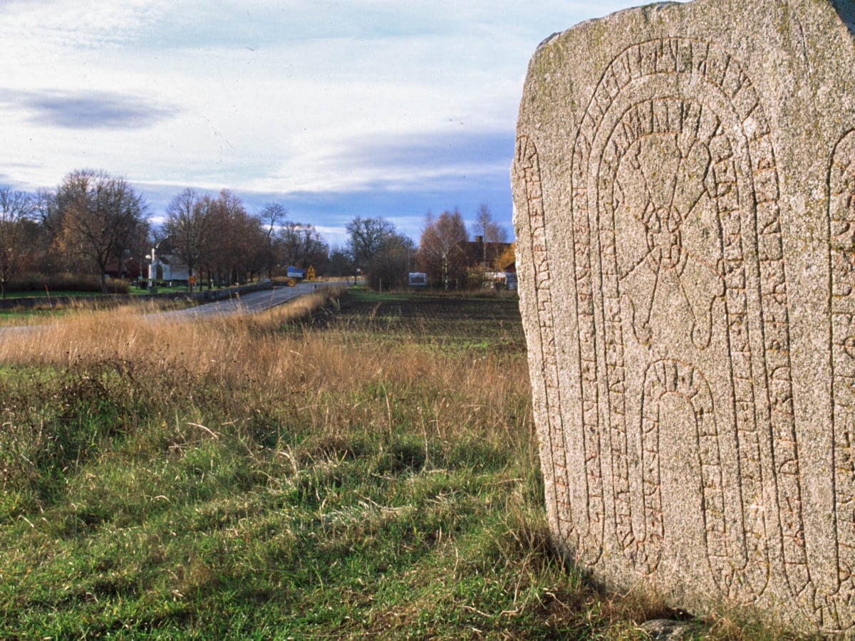 Landskap med en runsten i förgrunden.