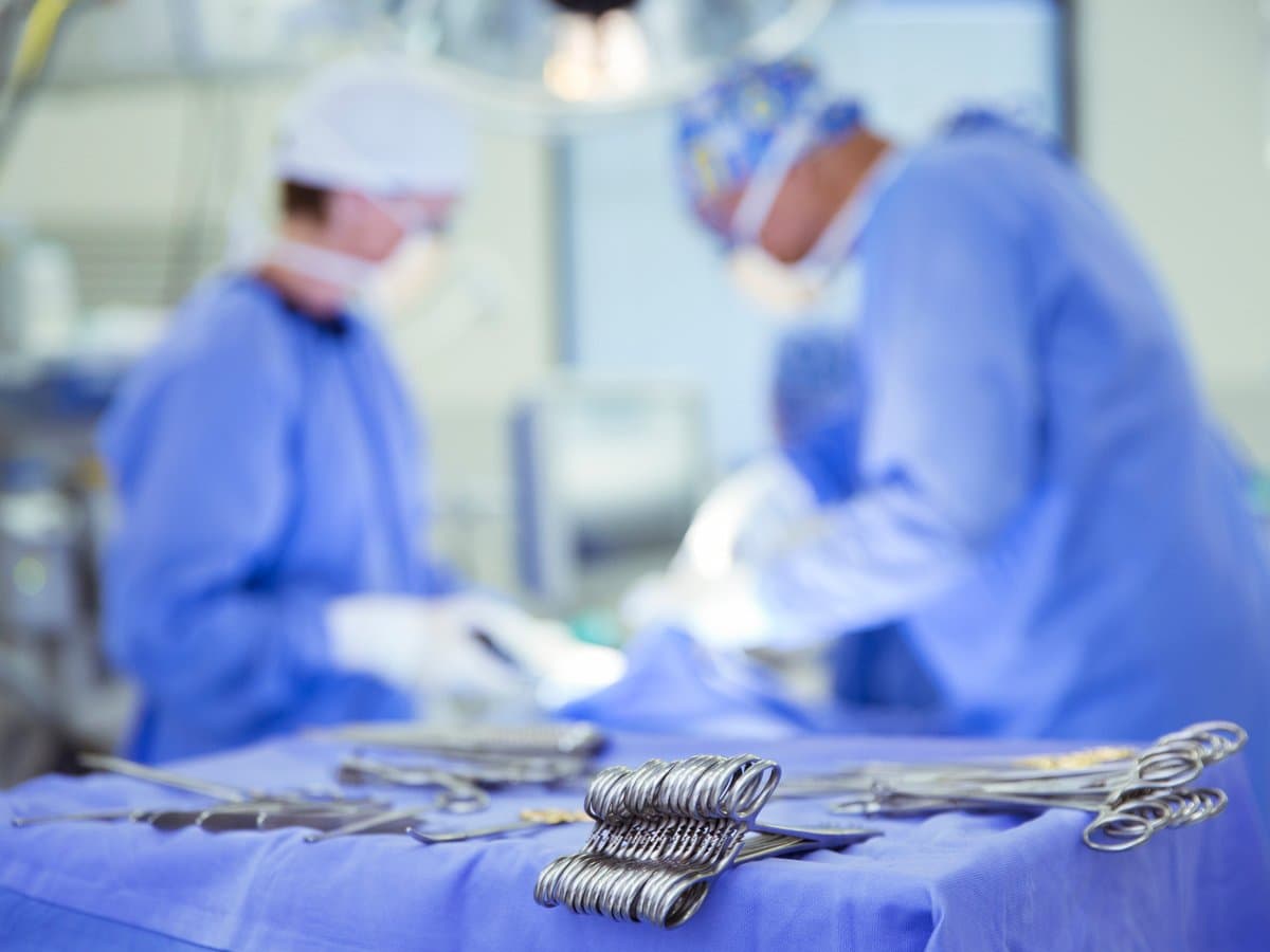 Kirurger klädda i blått med munskydd som opererar en patient.