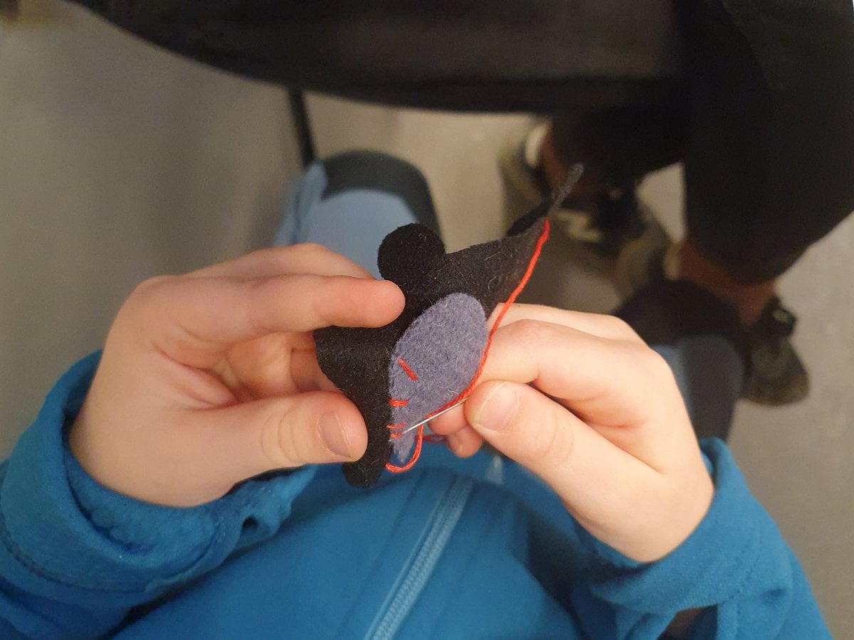 Två barnhänder som syr med röd tråd.