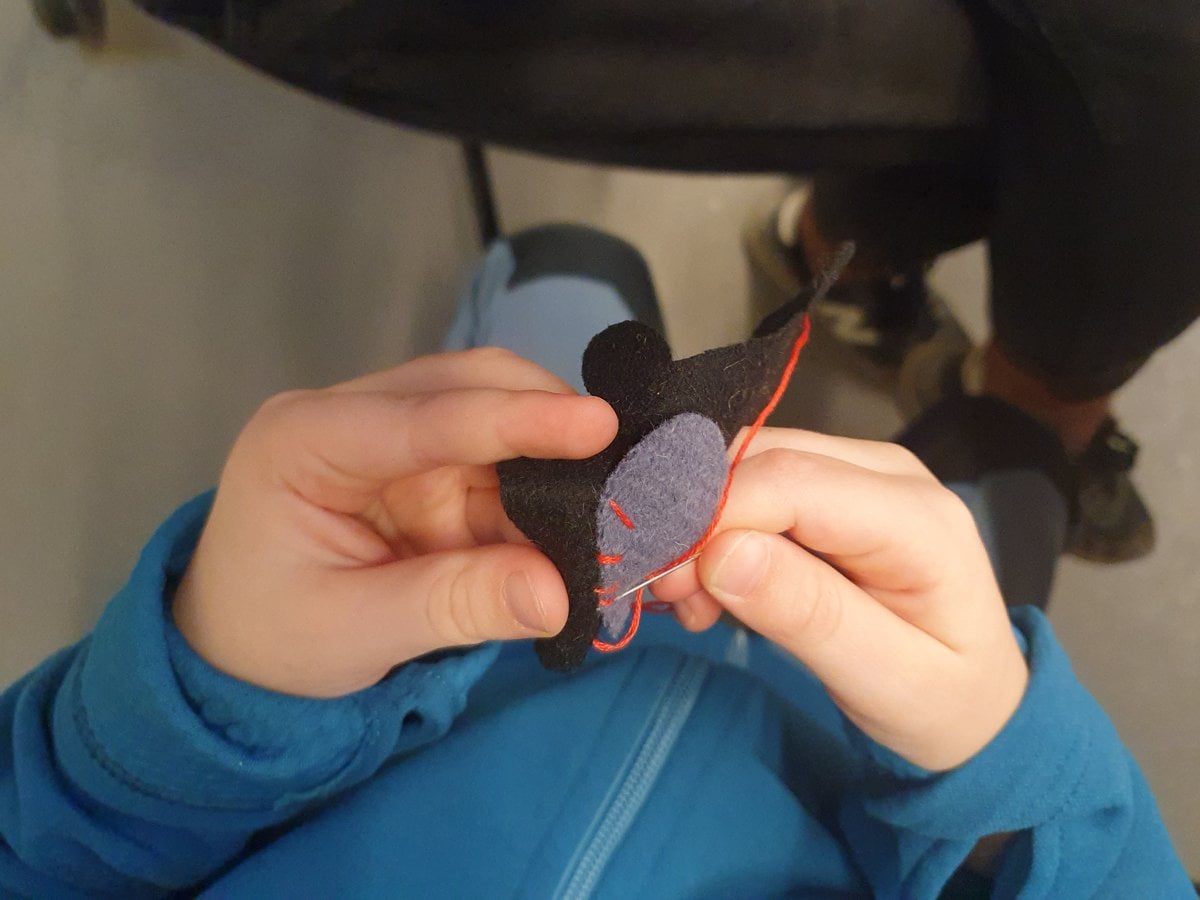 Två barnhänder som syr med röd tråd.