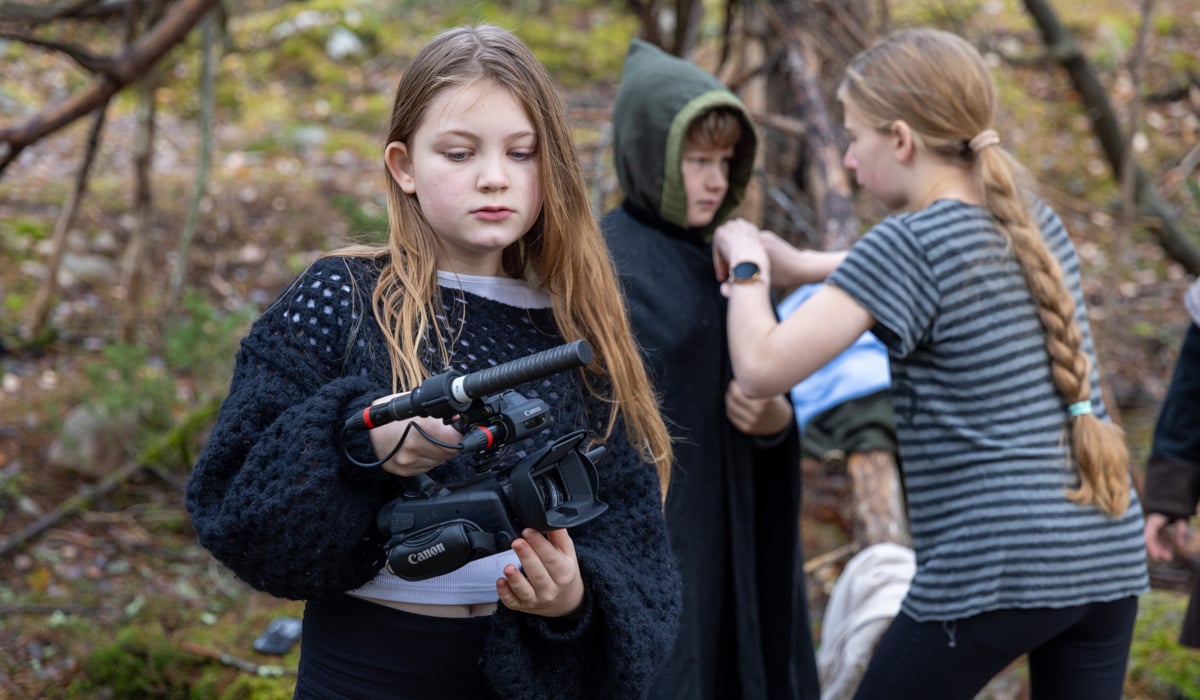 Tre barn som gör film tillsammans. En flicka håller i en videokamera och en annan rättar till ett plagg på pojken som ska bli filmad.