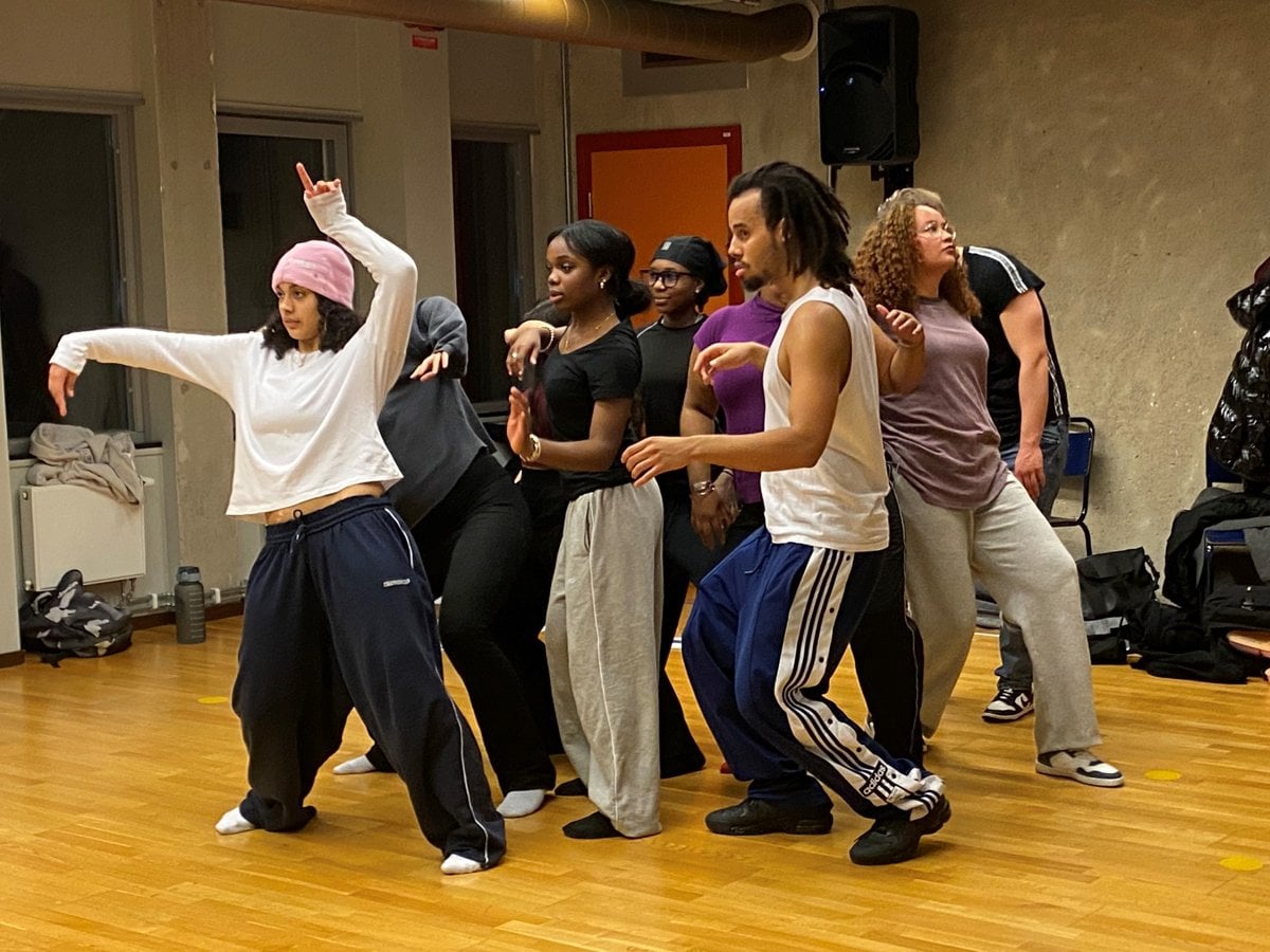 En grupp unga människor tränar dans  i en sal med trägolv.