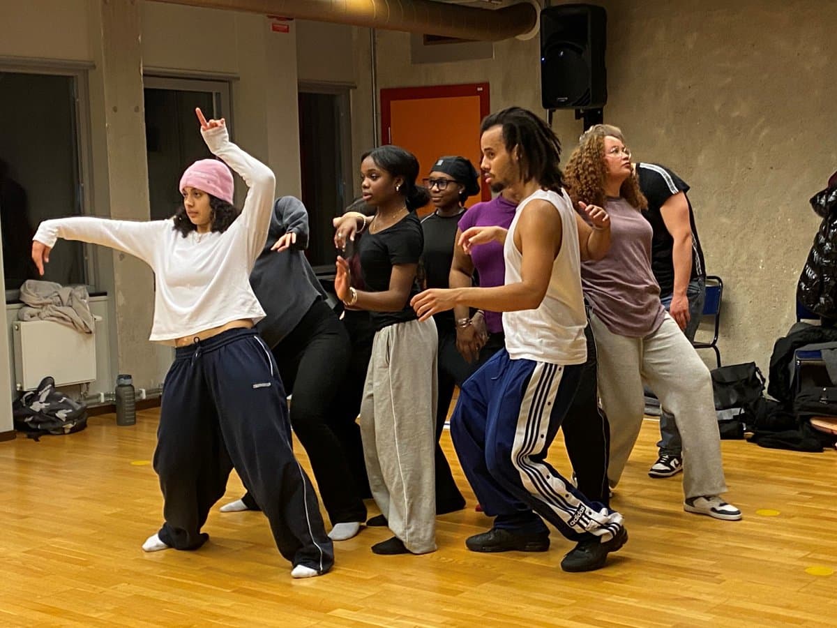 En grupp unga människor tränar dans  i en sal med trägolv.