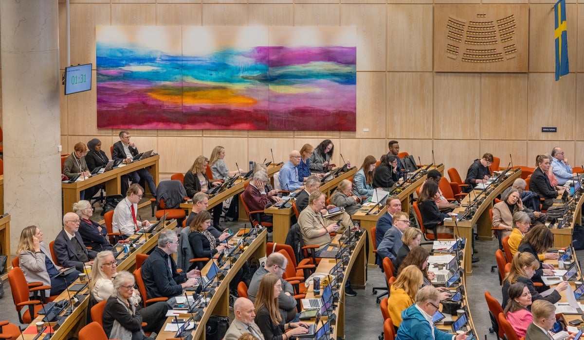 En grupp människor som sitter vid bord i landstingssalen.