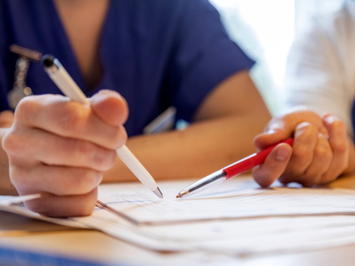 Närbild på två personers händer. Händerna håller i varsin penna som pekar mot ett papper.