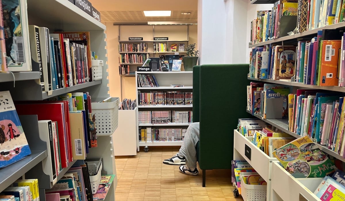 Ett bibliotek där en person läser i en fåtölj. Personen är dold men benen sticker ut framför fåtöljen.
