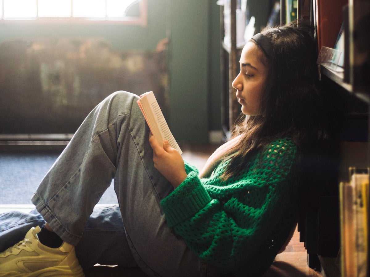 Flicka sitter och läser lutad mot en bokhylla