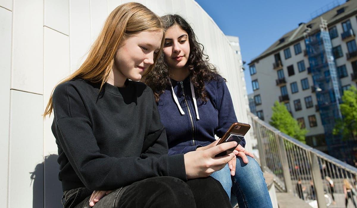 Två tjejer umgås med en telefon i ena handen