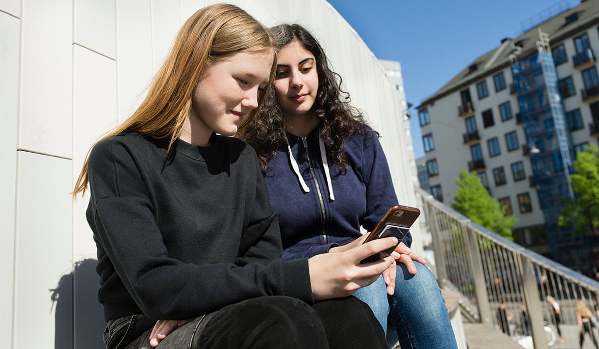 Två tjejer umgås med en telefon i ena handen