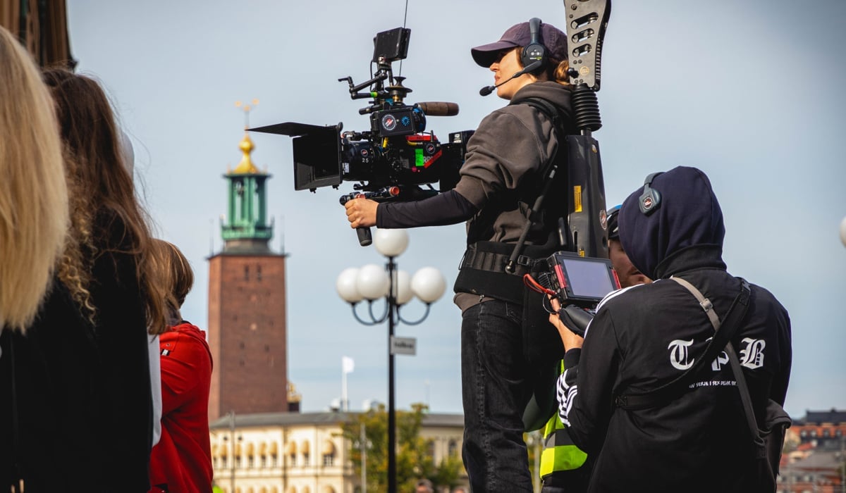 Filmfotograf med kamera i förgrunden, Stockholms stadshus i bakgrunden.