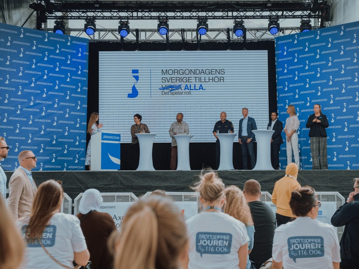 Bild från Järvaveckan 2023. Bild över paneldebatt på Järvaveckans stora scen. Paneldeltagare och moderator syns, med publik i förgrunden.