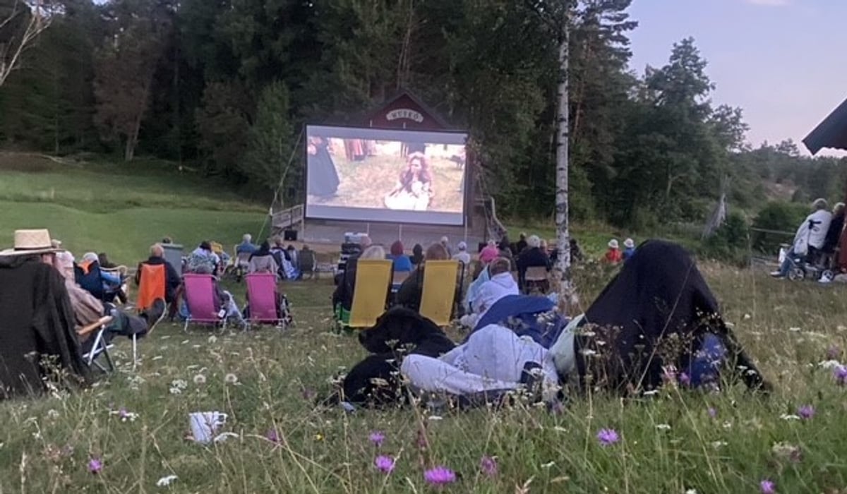 En grupp människor som sitter på ett fält och tittar på en film.