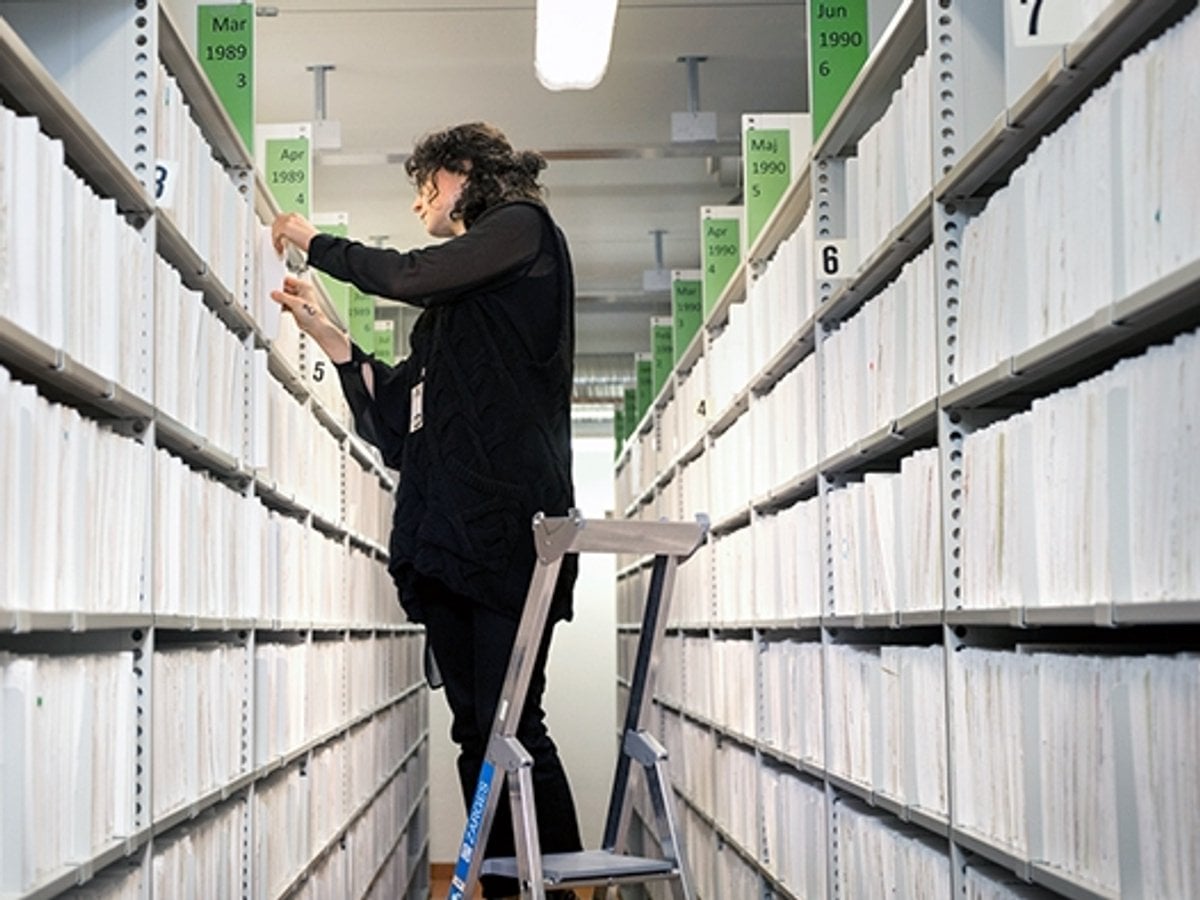 Arkivarie på stege mellan hyllor på arkivet.