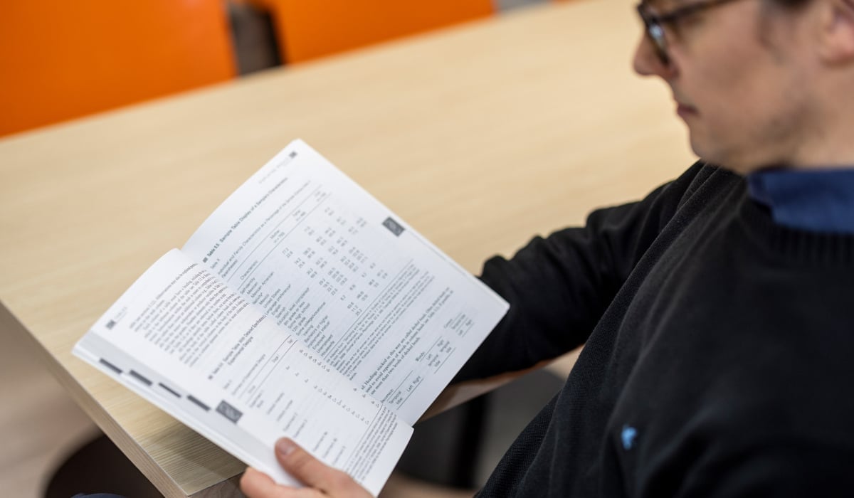 Foto på en person som sitter vid ett bord och läser i en bok.