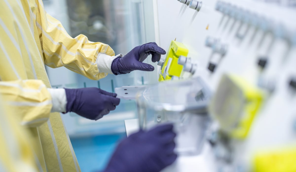 Foto på personer i ett labb. På bilden syns bara personernas händer iklädda handlar.