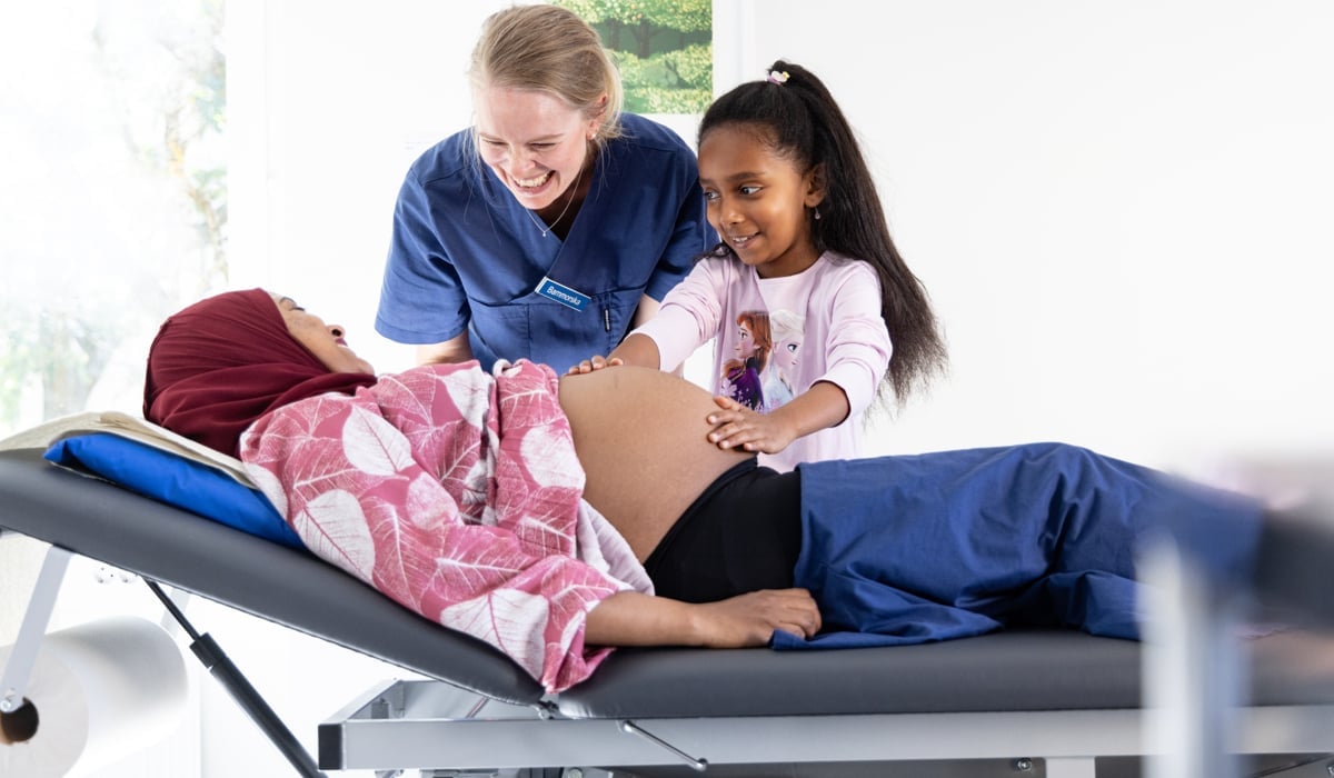 En gravid kvinna ligger på en brist och blir undersökt på magen av en barnmorska.
