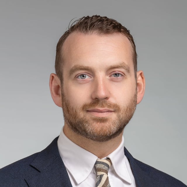 En man i kostym och slips poserar för en bild.