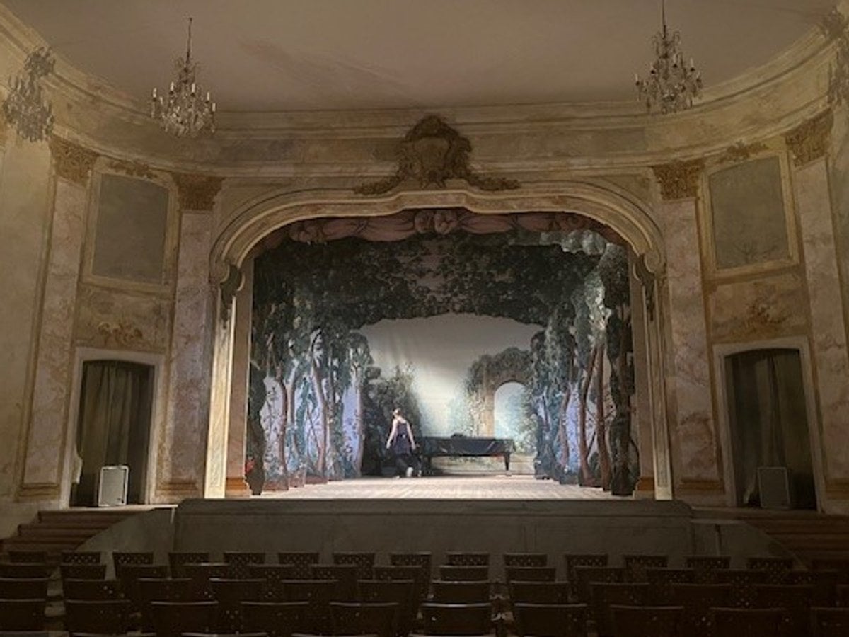 Scenrummet i Ulriksdals slottsteater. Stolar framför en scen i 1700-talsstil med kulisser och scenljus