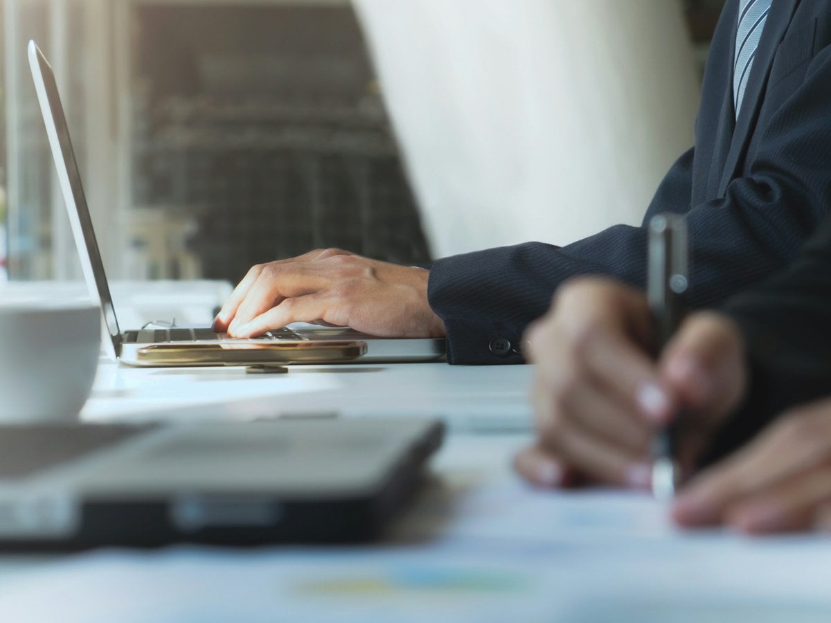 Närbild på händer på personer som skriver för hand och på dator