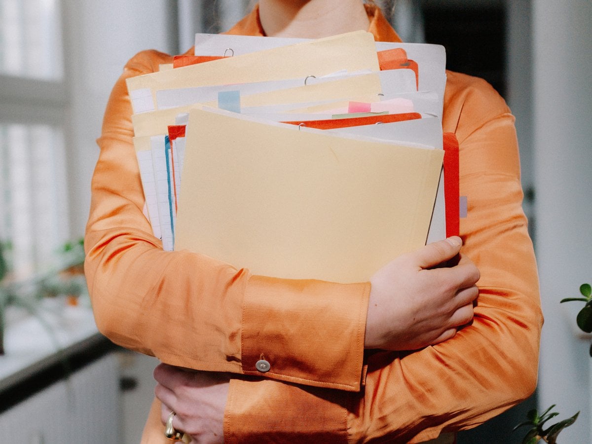 En kvinna står med en bunt papper och mappar i famnen i kontorsmiljö