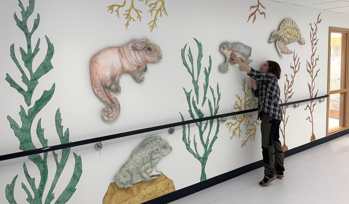 Ida sträcker sig mot figur på vägg.