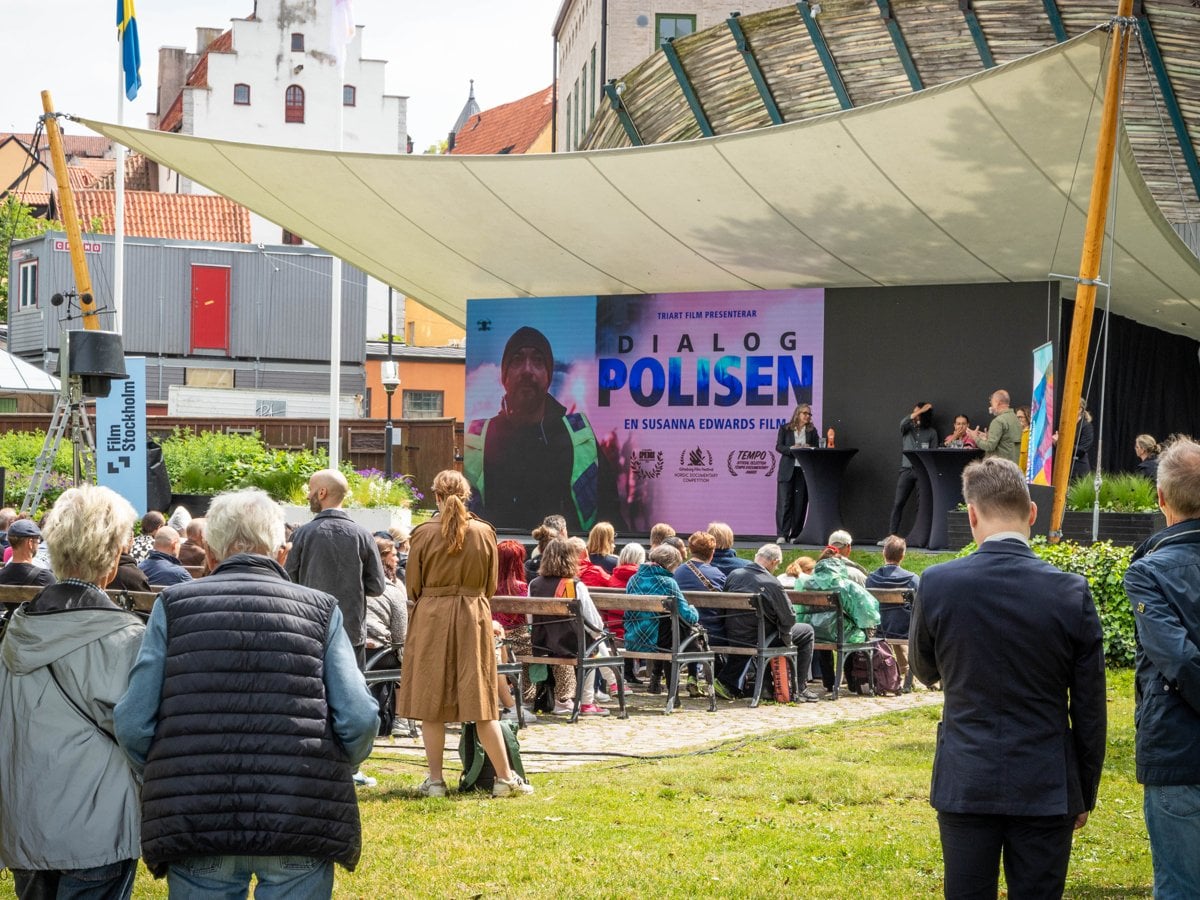 Folksamling framför en scen med en skylt med texten "Dialogpolisen"