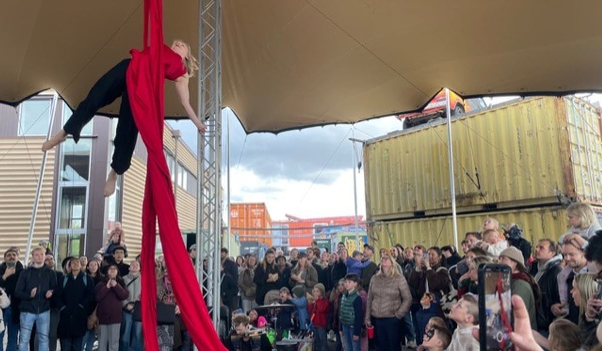 En kvinna hänger högt upp i luften i ett rött cirkusrep framför en folkmassa.