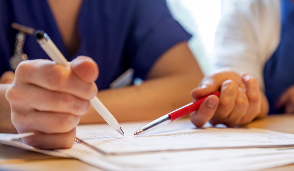 Bild på två personer. Fokus på deras händer där de skriver på ett gemensamt papper.