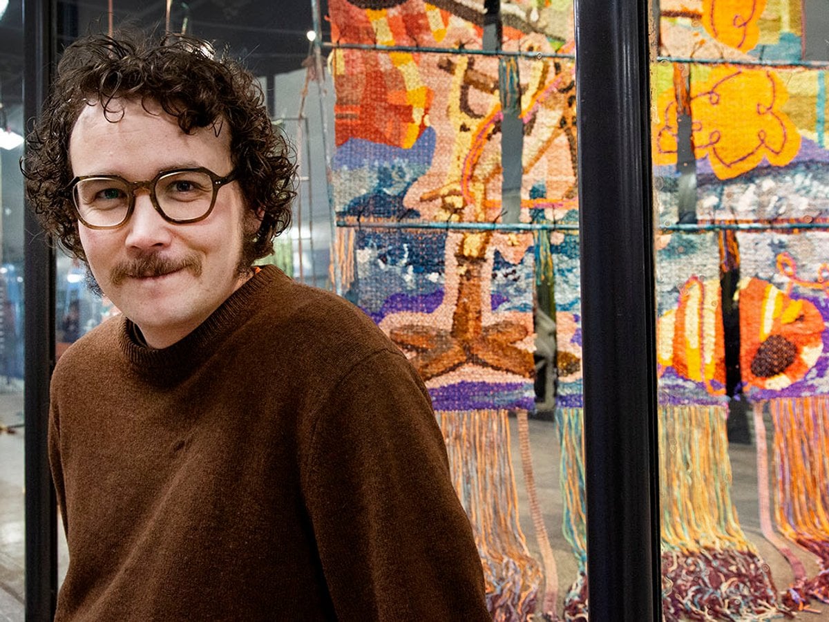 Gustav lutar sig mot glasmontern. Vävar hänger i tre nivåer på en ställning inuti montern.