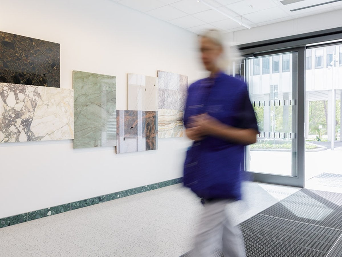 Stenplattor i olika färger på vägg i en entré. En person i vårdkläder passerar