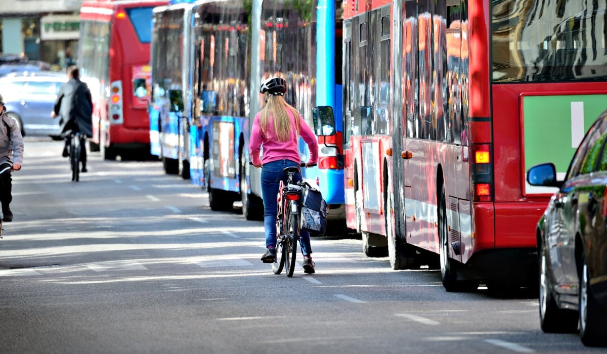En kvinna cyklar på en gata bredvid en buss.