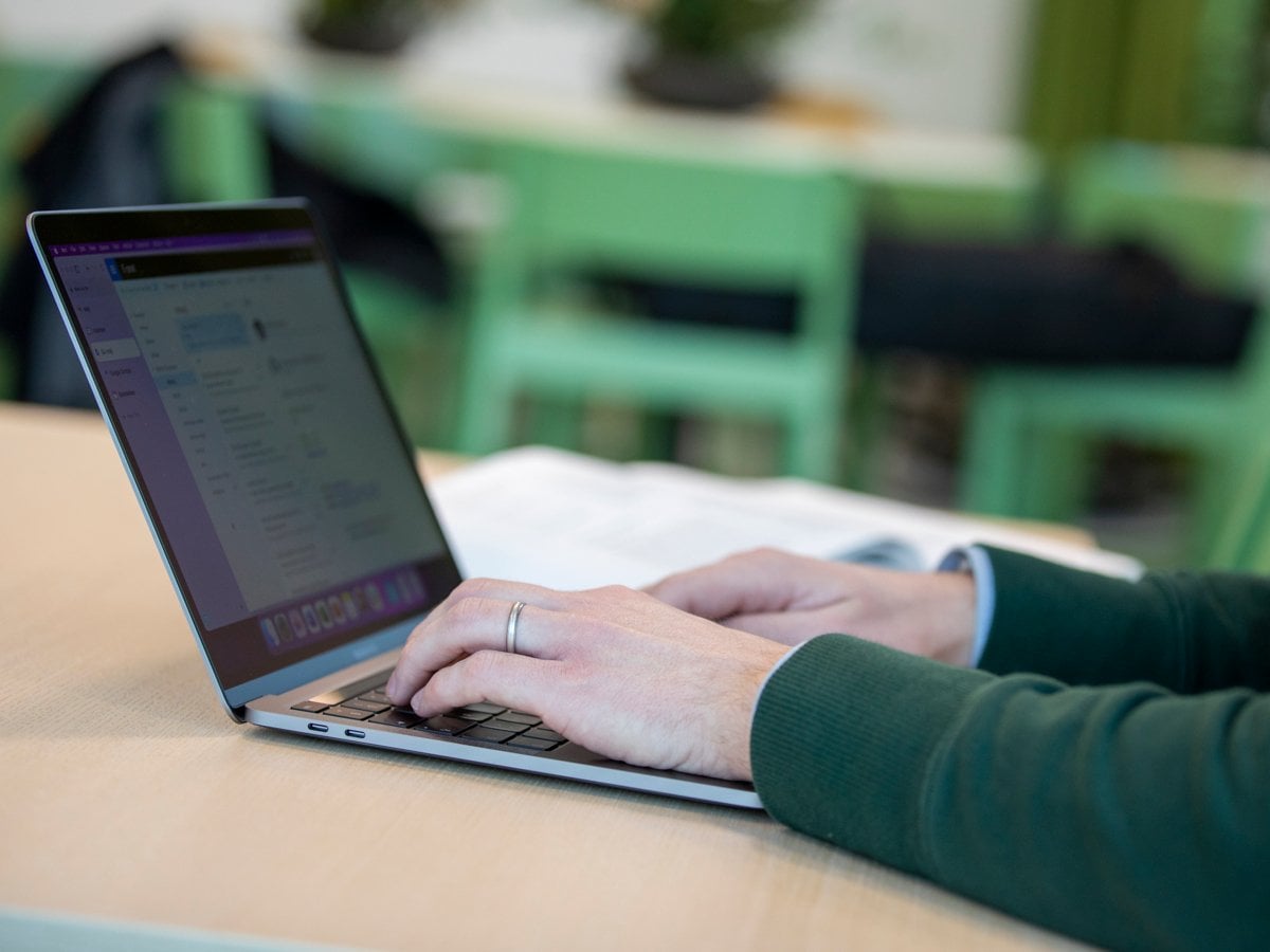 En man med grön stickad tröja skriver på sin laptop.