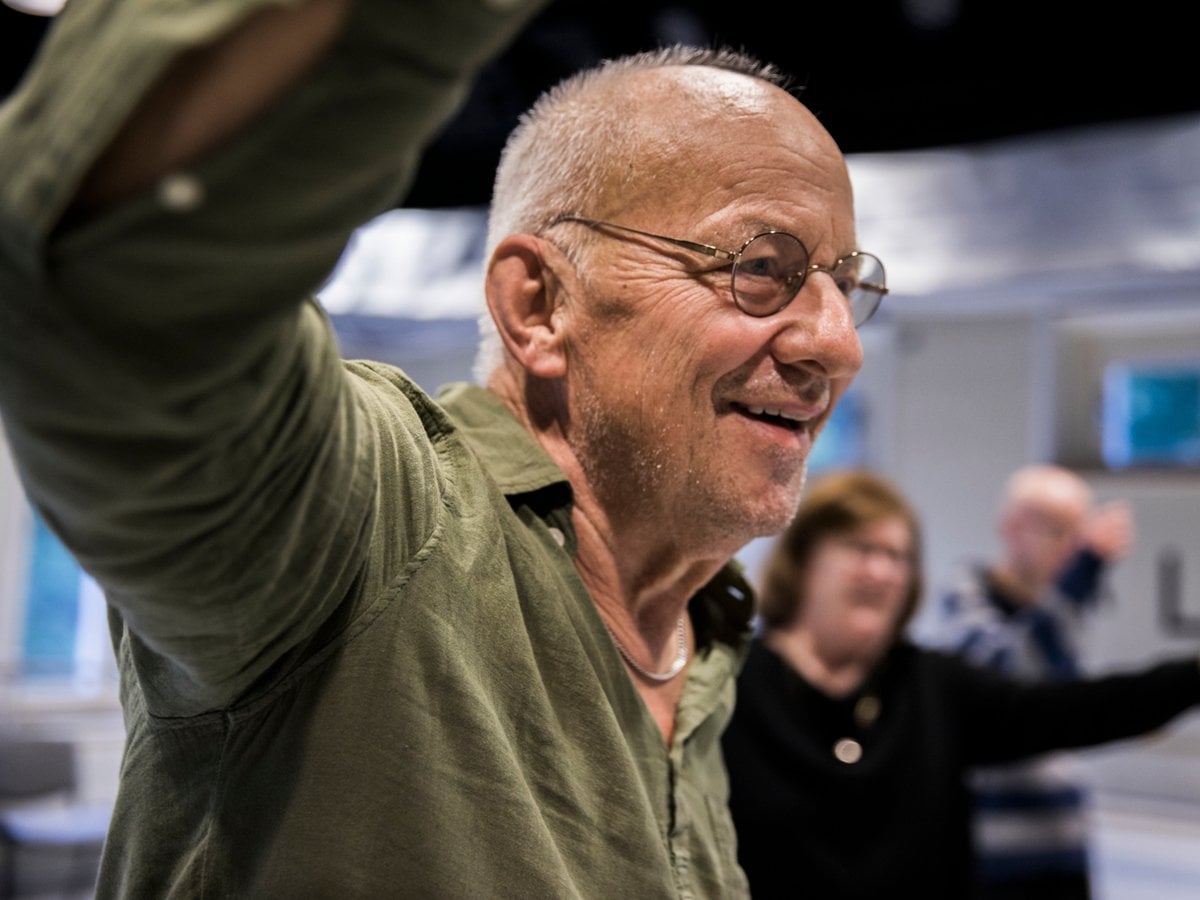 Äldre man dansar i grupp. Han ser glad ut.