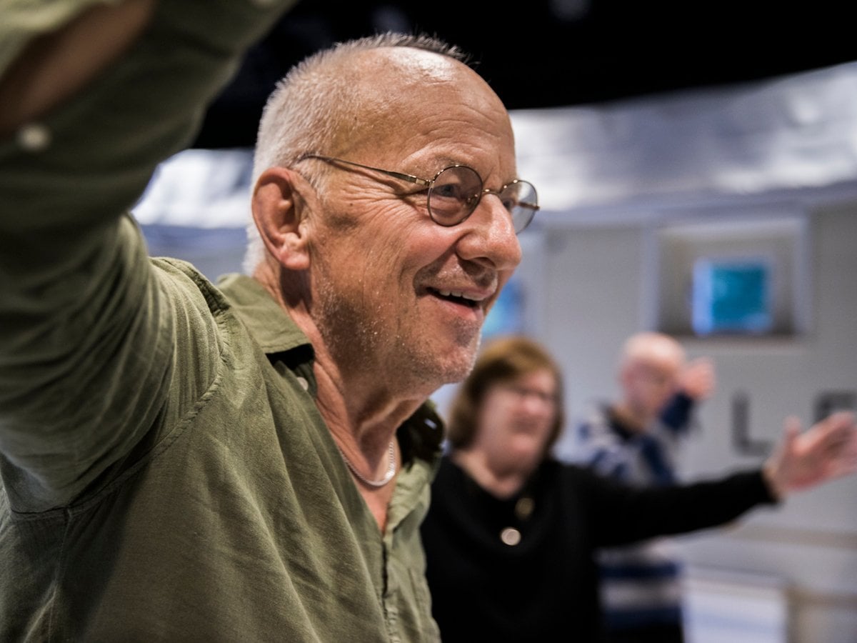 I förgrunden en äldre glad man som dansar. I bakgrunden flera äldre personer med armarna i luften.