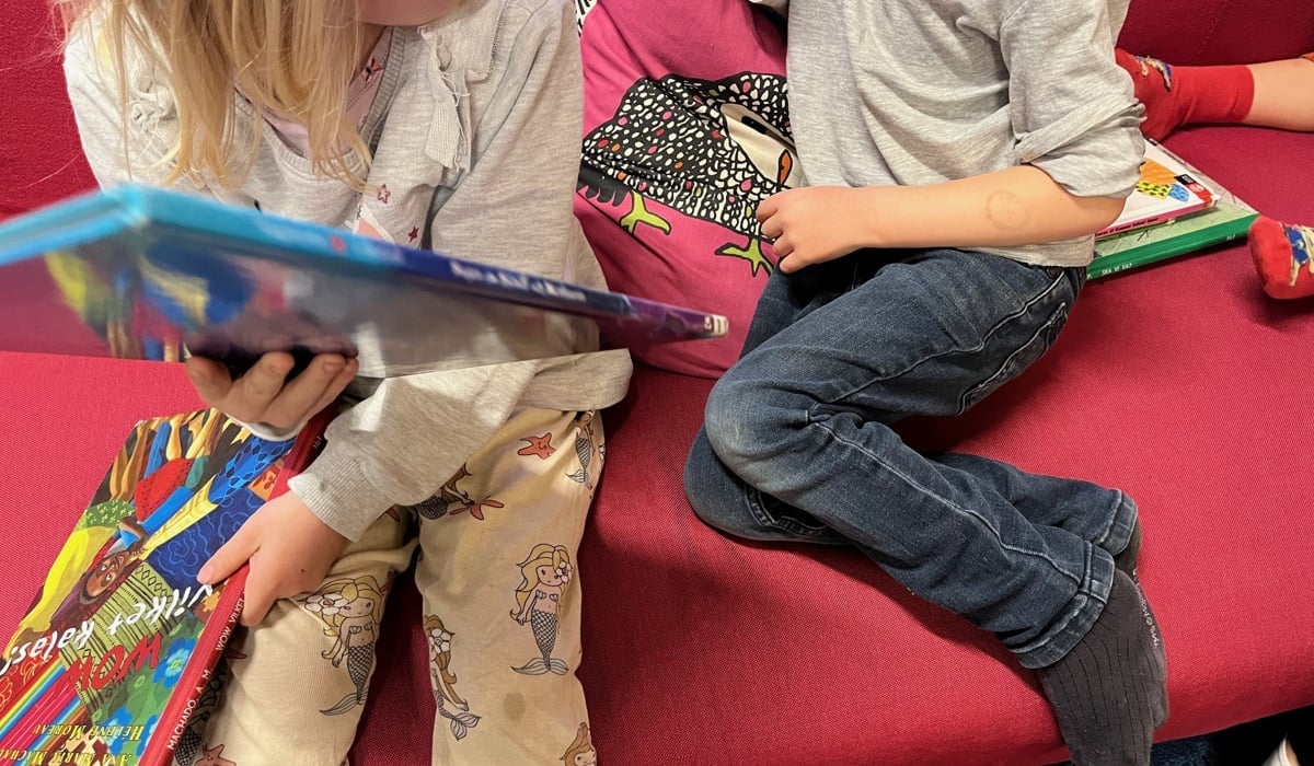 Två barn på bibliotek i en rosa soffa.