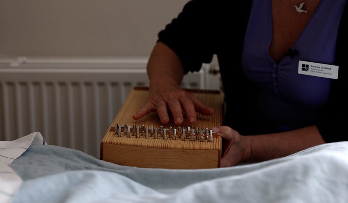 Inzoomat fotografi av händer och ett stränginstrument vid en sjukhussäng.