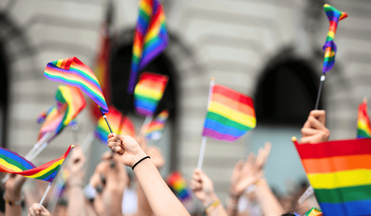 Många händer i luften som håller i prideflaggor