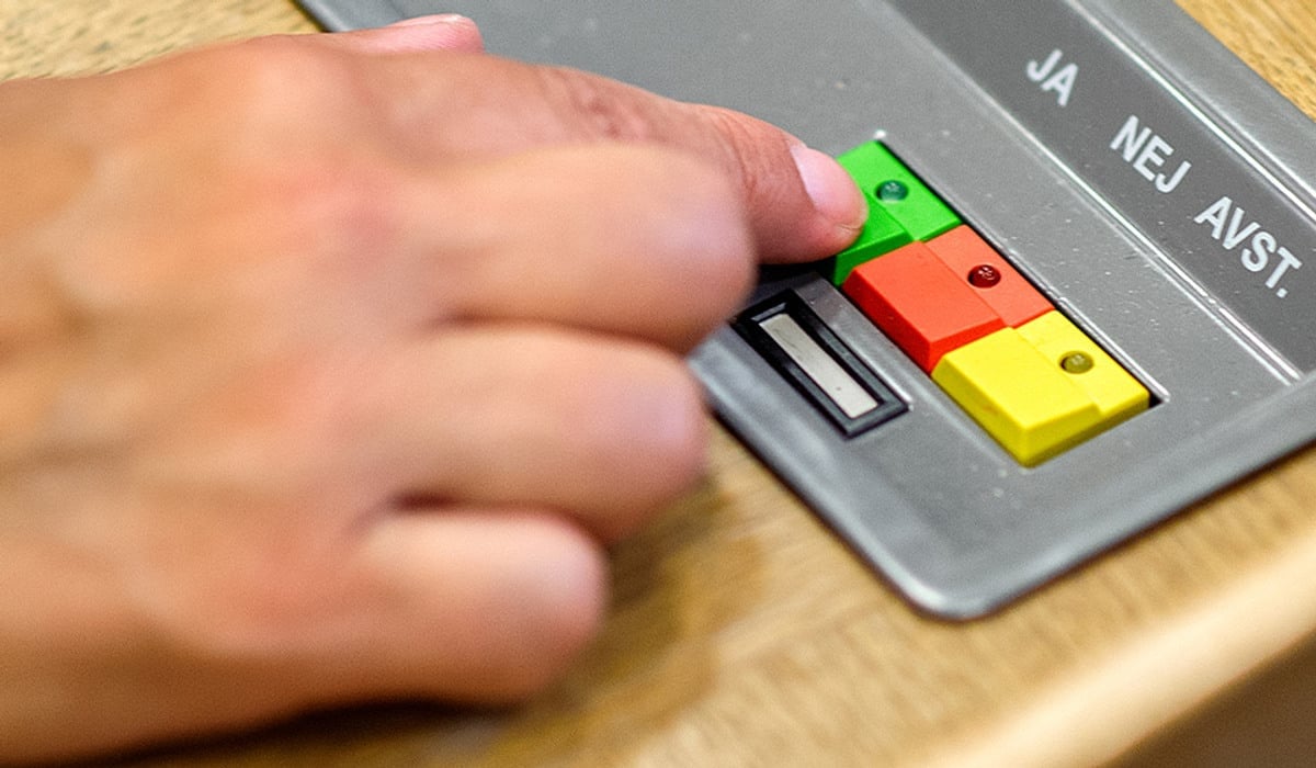 En persons hand på en tryckknapp som använda för att rösta i regionfullmäktige.