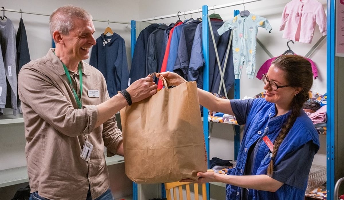 En man och en kvinna överlämnar en pappkasse med kläder mellan sig.