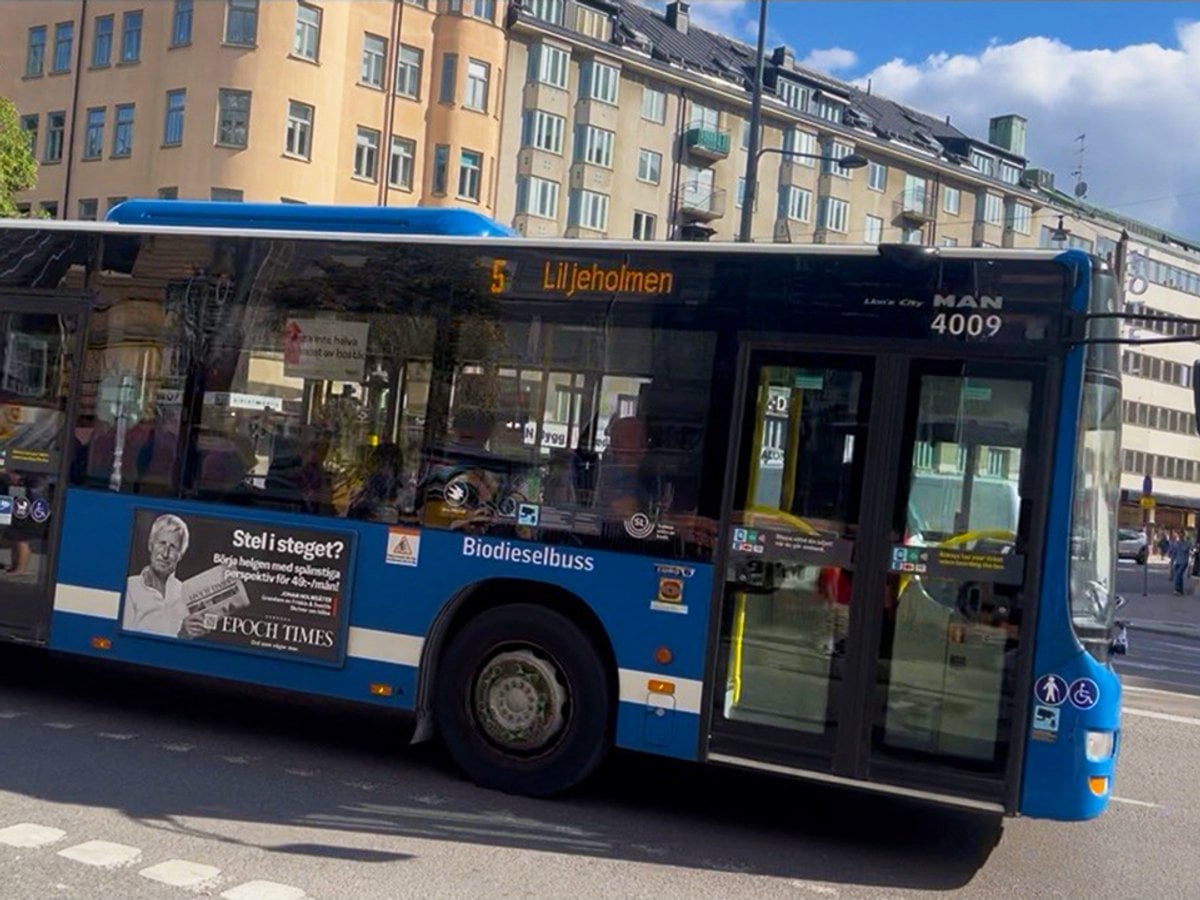 En blå buss, linje 5, kör längs en gata bredvid höga byggnader.