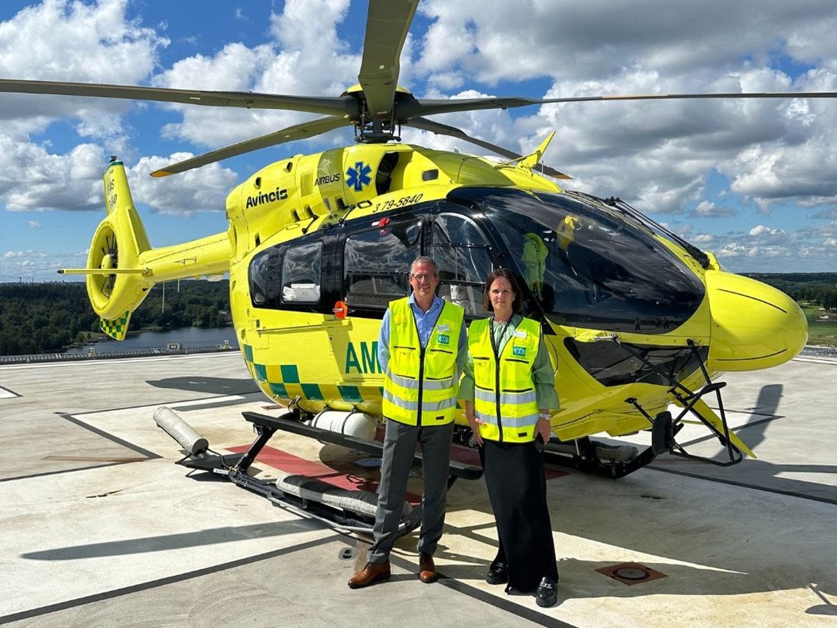 Två personer står framför en helikopter på en helikopterplatta.