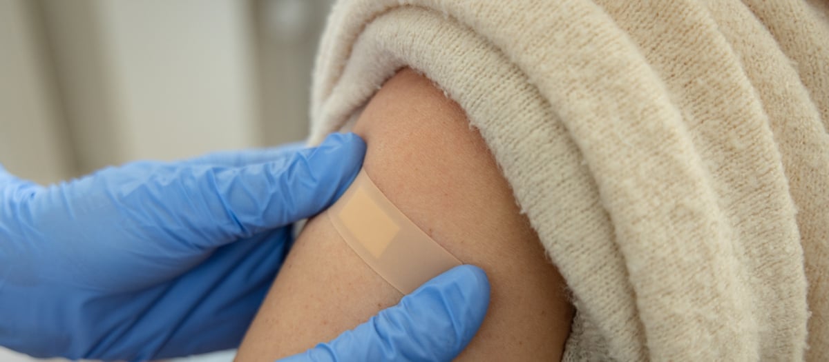 Vårdgivares händer. Patient får plåster på överarmen efter vaccination.