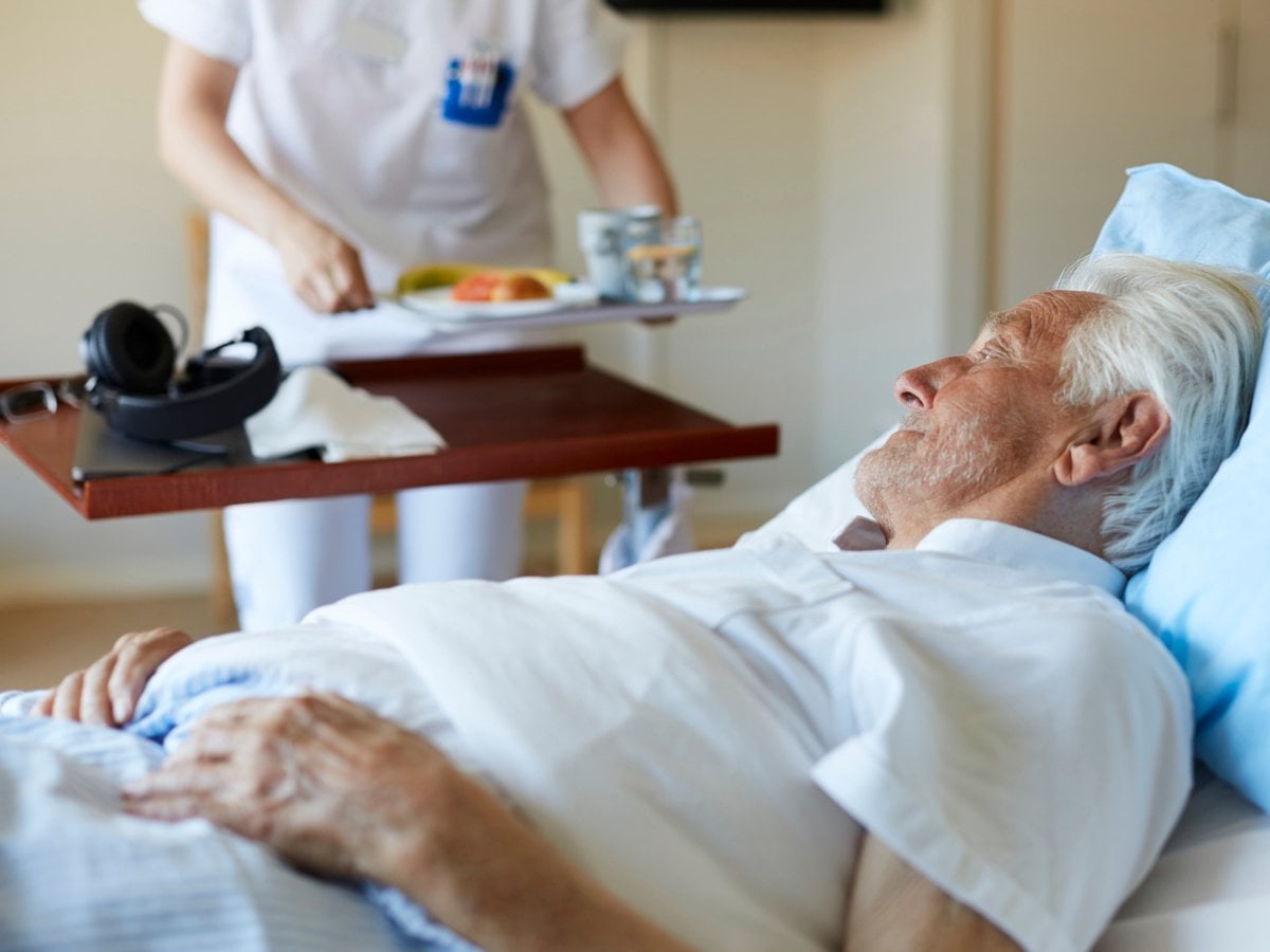 Äldre patient i sjukhussäng blir serverad mat på en bricka