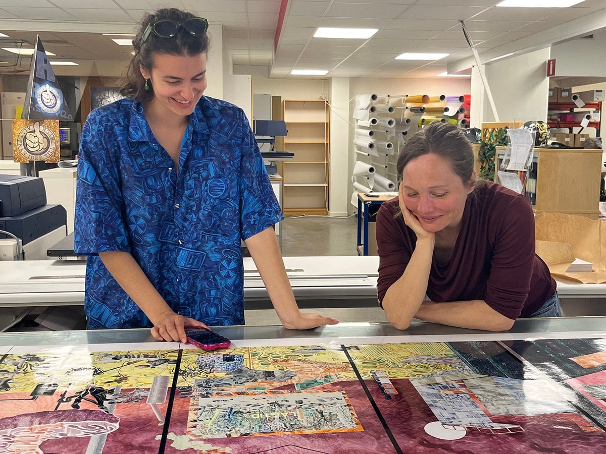 Yuvia och Ellisif tittar på bilder som ligger på ett bord inför utställningen på Skanstull.